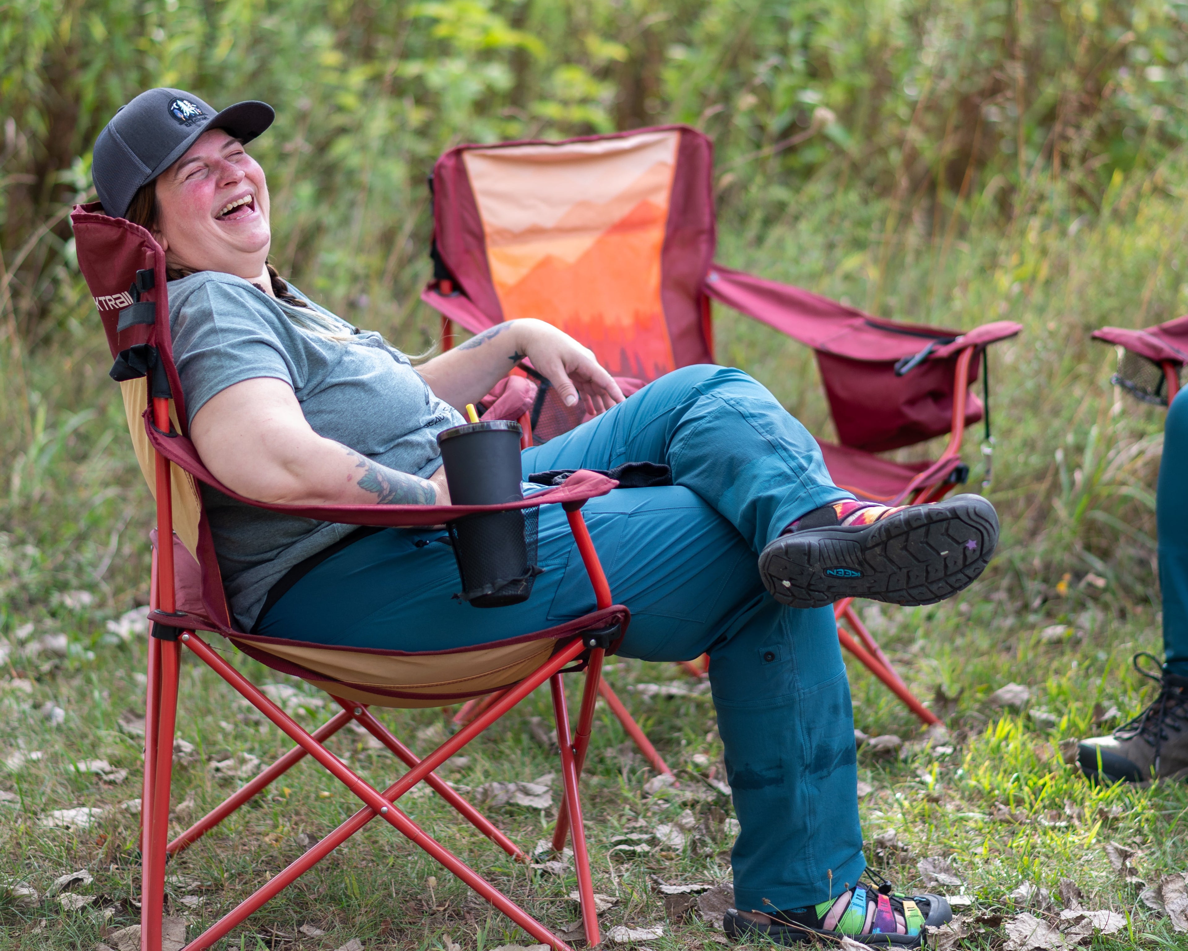 A woman sitting in a camping chair laughing in hiking gear. 