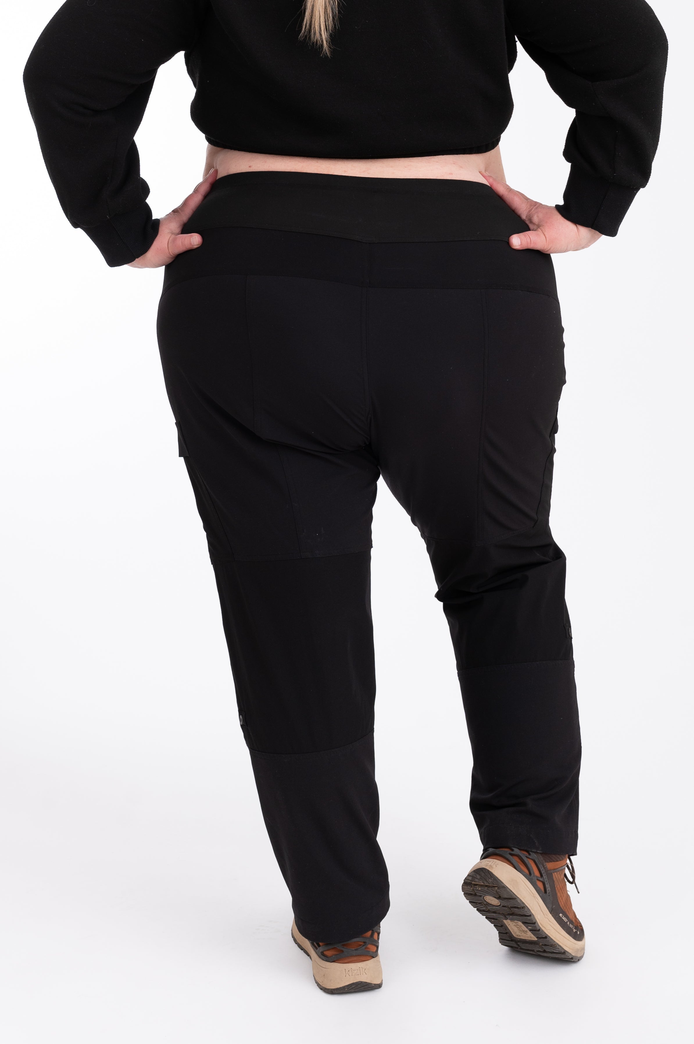 Person wearing black hiking pants and crop top on a white background