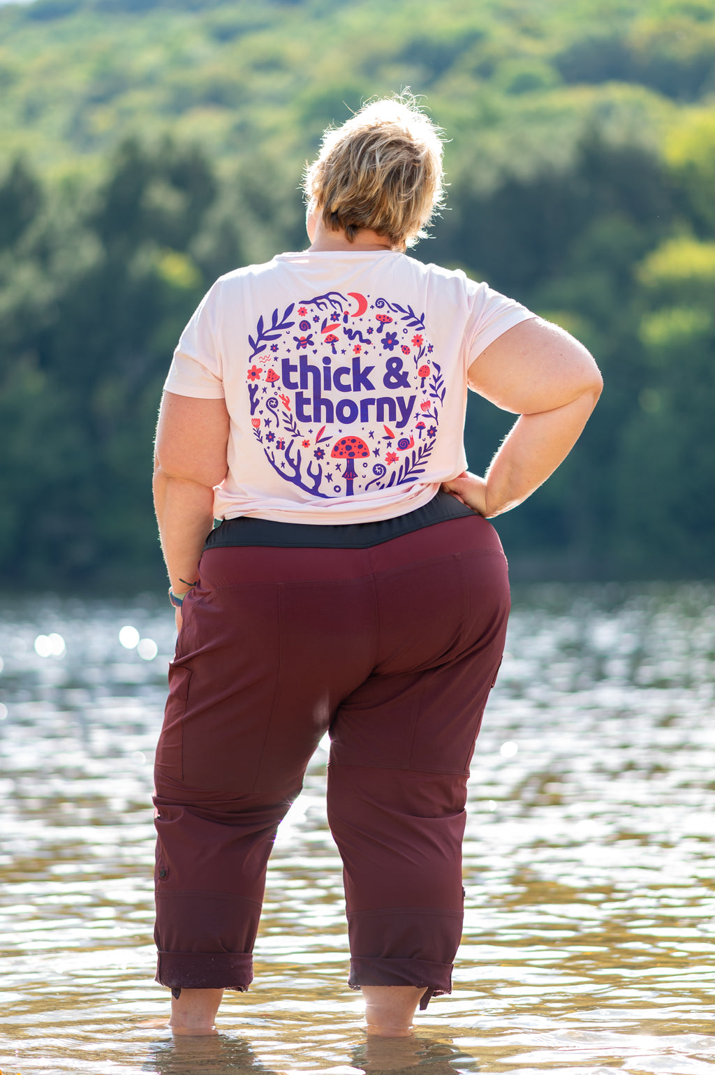 Person wearing a shirt with 'thick & thorny' design by a lake