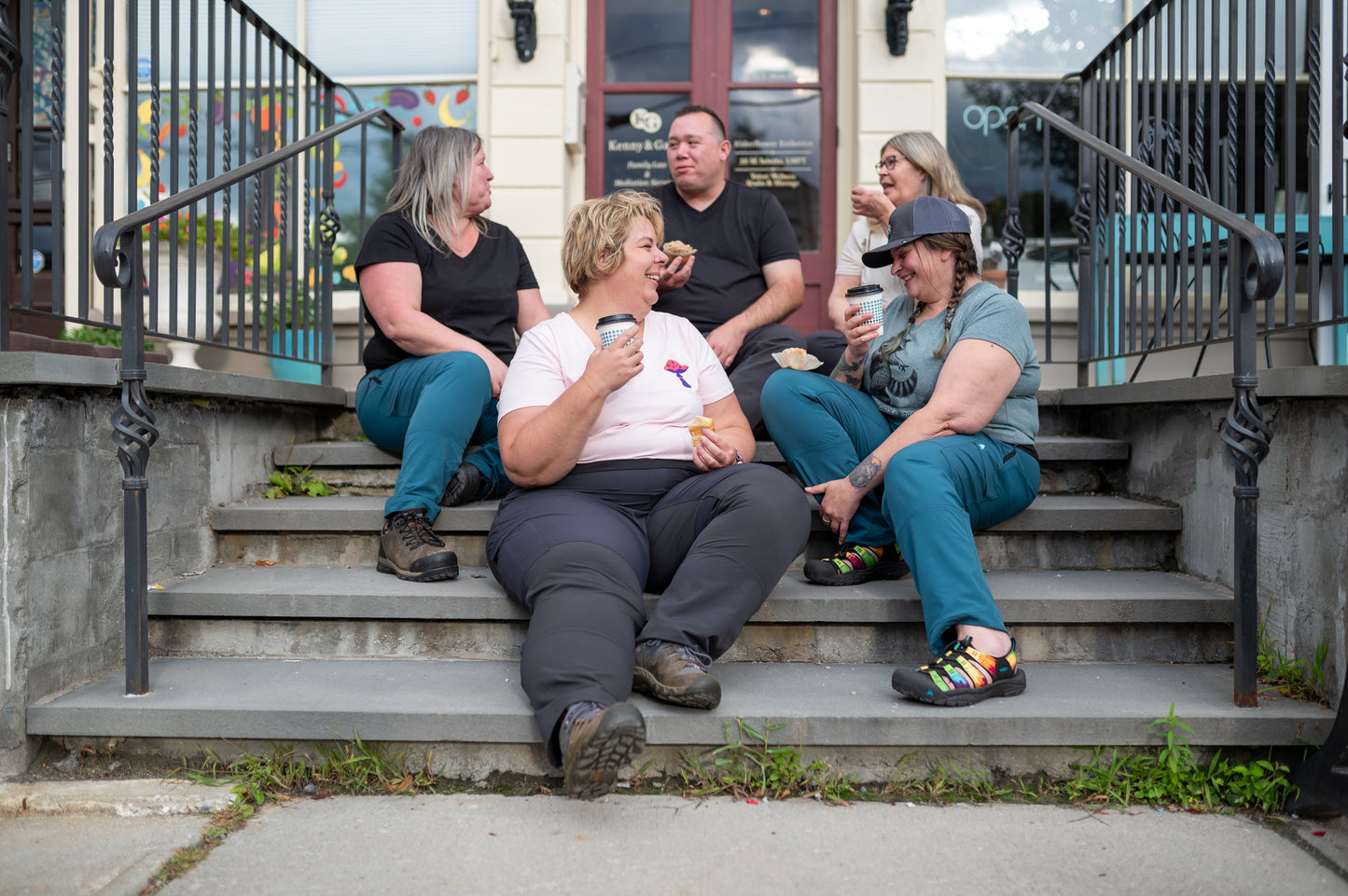 Group of people sitting on steps outdoors, drinking coffee and eating pastries.