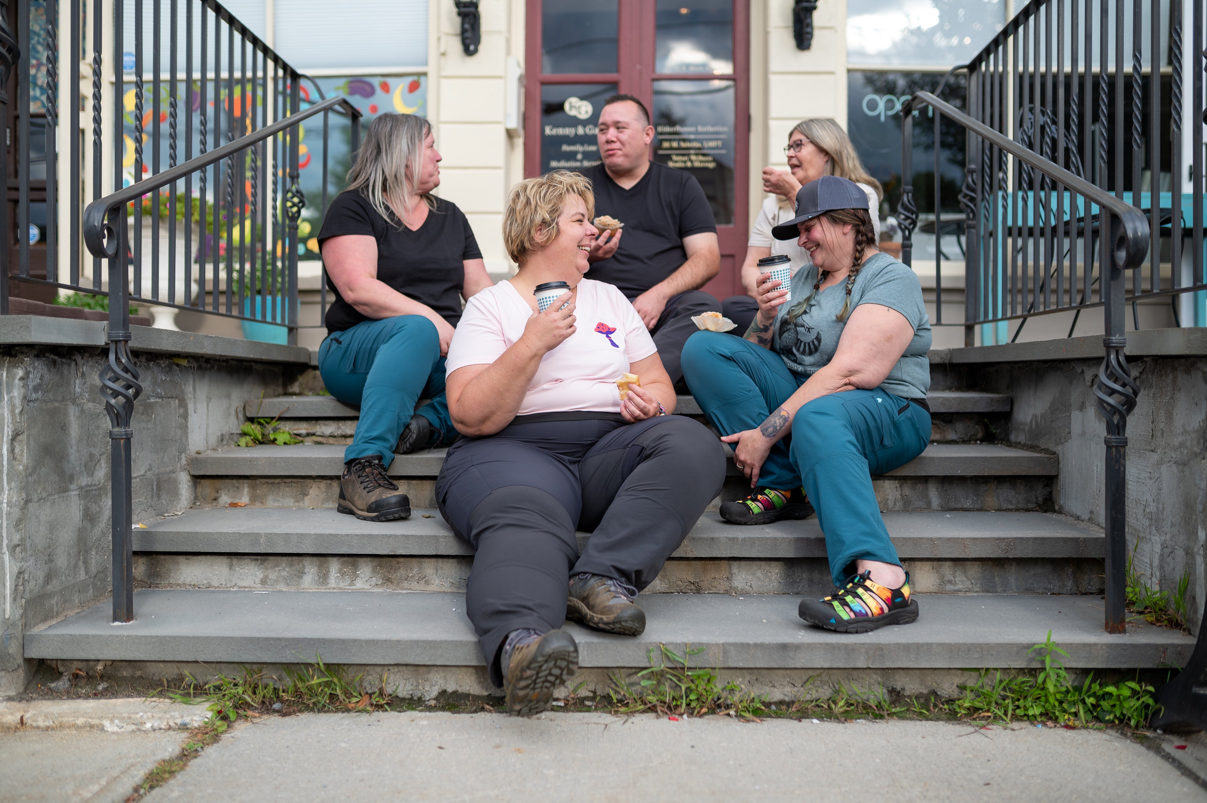 Group of people sitting on steps outdoors, drinking coffee and eating pastries.