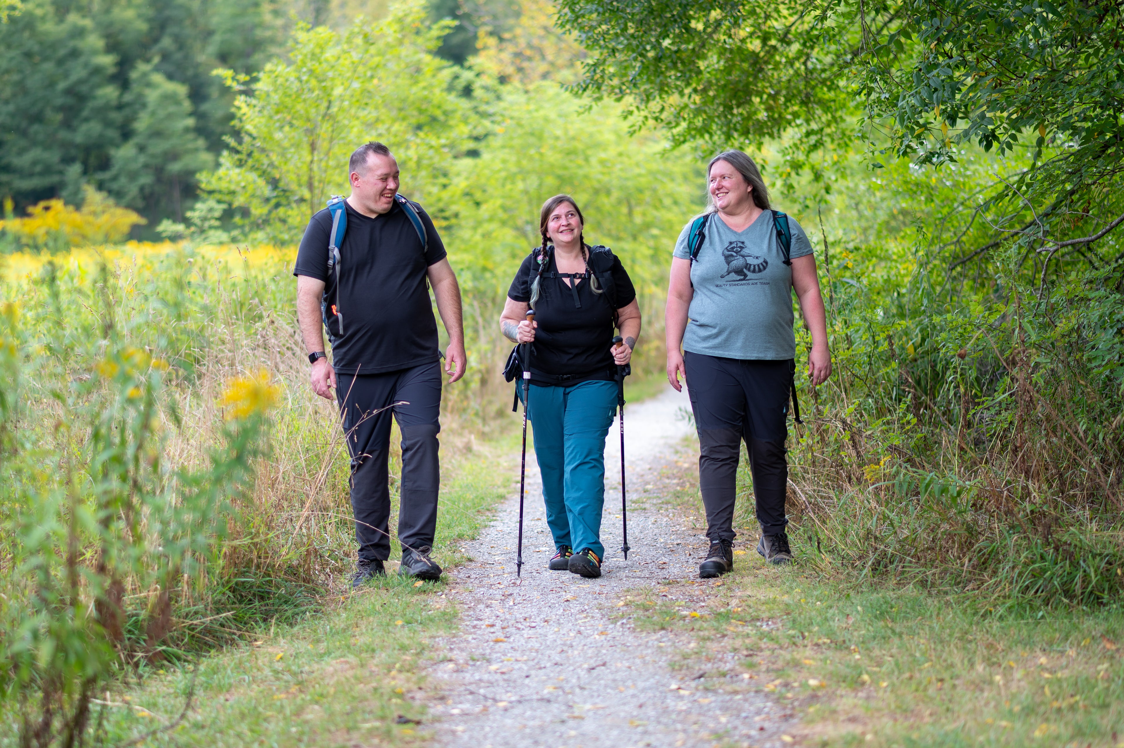 Three people hiking on a trail surrounded by foliage and wildflowers